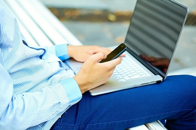 Young man working with laptop, man's hands on notebook computer, business person in casual clothes in the street