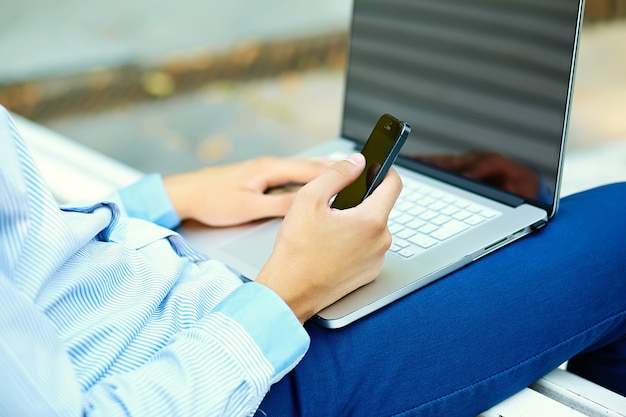 Young man working with laptop, man's hands on notebook computer, business person in casual clothes in the street