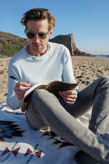 Young man writing in his agenda at the beach