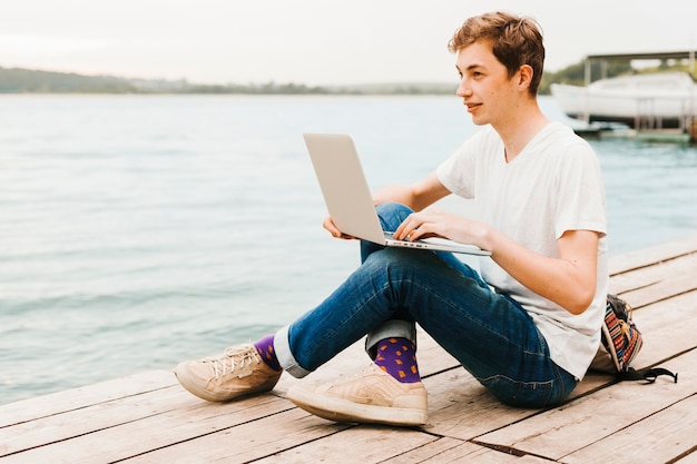 Foto gratuita scrittura del giovane sul computer portatile dal lago