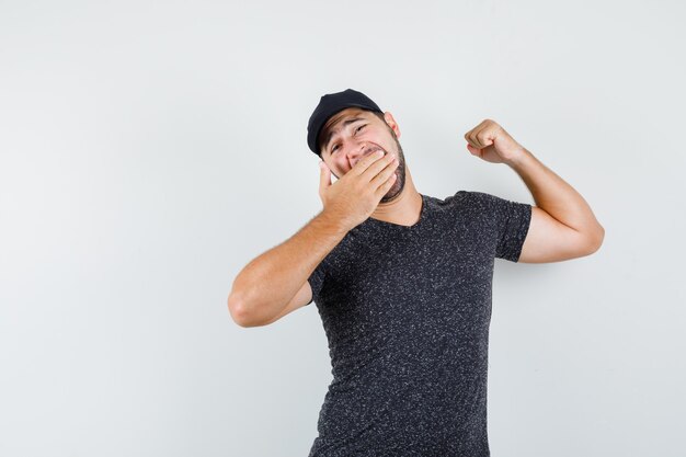 Young man yawning and stretching in t-shirt and cap and looking sleepy