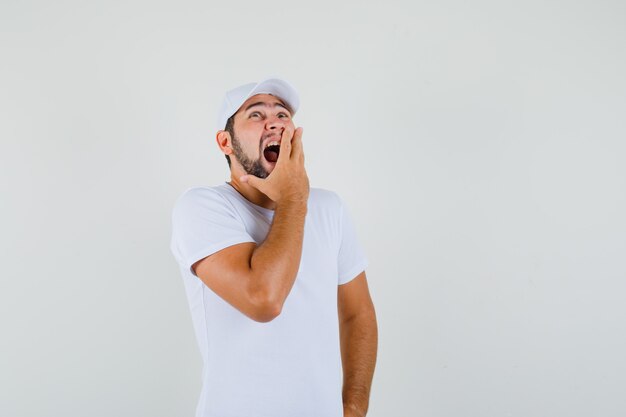 Young man yawning while looking up in white t-shirt and looking sleepy