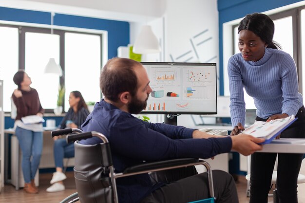 Young manager woman working with financial documents checking graphs talking with paralysed team leader with disabilities