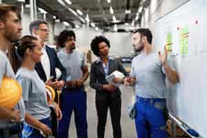 Free photo young manual worker presenting new business strategy to company managers and his colleagues in a factory