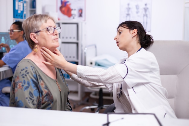 Young medic palpating neck of senior woman, elderly patient visiting doctor at hospital checking thyroid throat touching health at clinic. Healthcare specialist, medicare, treatment medical concept.