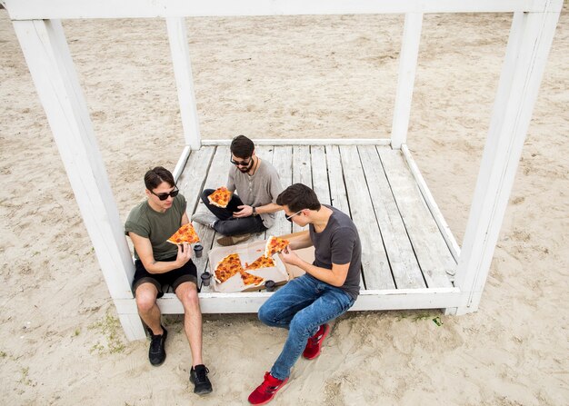 Giovani uomini che mangiano pizza sulla spiaggia