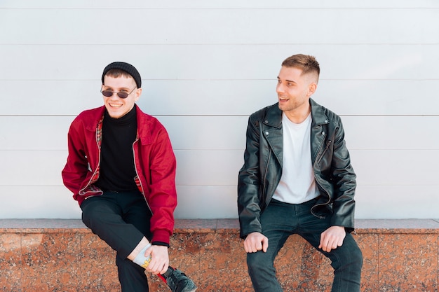 Young men sitting on parapet and smiling 