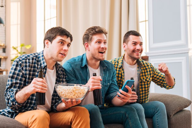 Young men sitting on sofa watching sport event on television at home