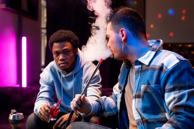 Young men vaping from a hookah indoors