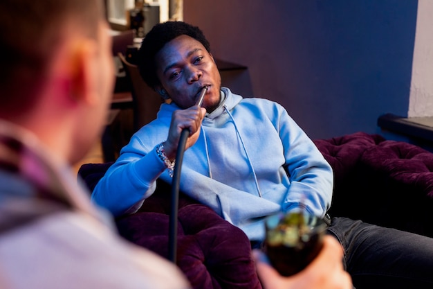 Young men vaping from a hookah indoors