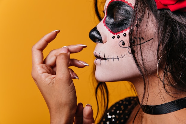 Young mexican girl with roses in her hair and skull-shaped art on face poses cute with her eyes closed