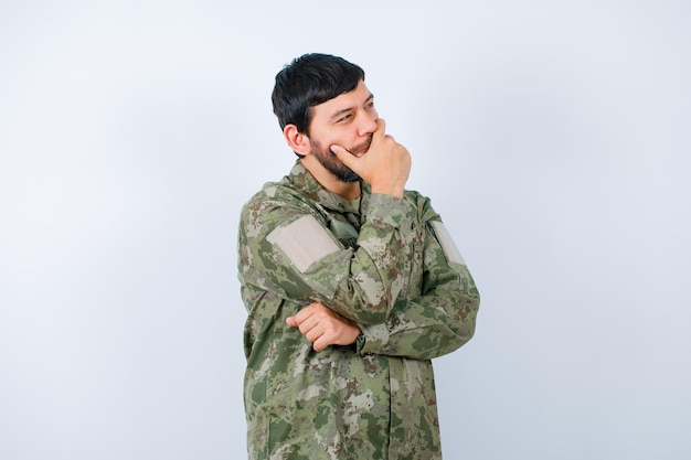 Young military man is thinking by holding hand on mouth and looking away on white background