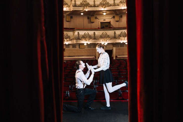 Free Photo young mime couple performing on stage seen through an open red curtain