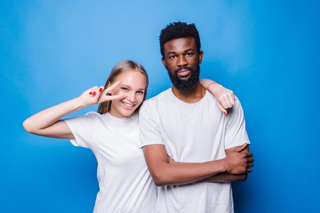 Young mixed couple with peace gesture isolated on blue wall