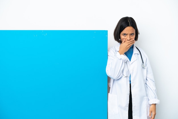 Молодая женщина-врач смешанной расы с большим плакатом, изолированным на белом фоне, прикрывает рот рукой