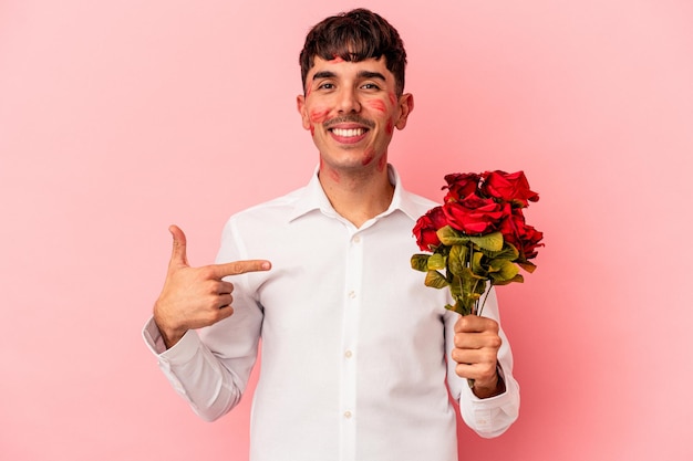 Young mixed race man holding a bouquet of flowers isolated on pink background person pointing by hand to a shirt copy space, proud and confident Premium Photo