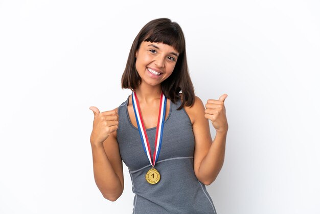 親指​を​上​に​向けて​ジェスチャー​と​笑顔​で​白い​背景​に​分離された​メダル​を​持つ​若い​混血​の​女性