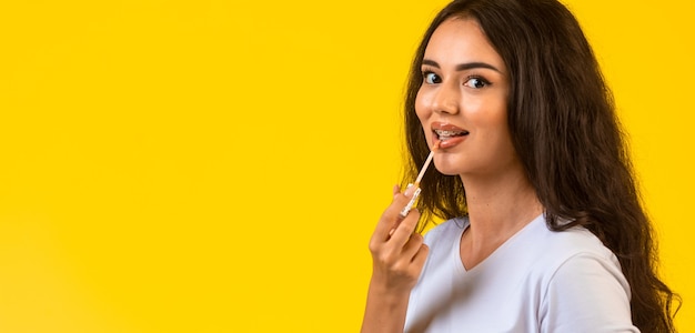 Young model applying lip gloss and smiling