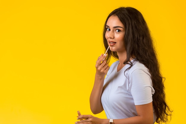 Young model applying lip gloss and smiling.