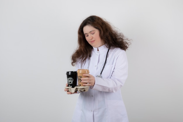 Giovane modella ragazza in uniforme bianca che tiene un cartone con tazze di caffè.