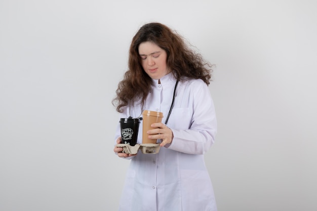 молодая модель девушка в белой форме, держа картон с чашками кофе.