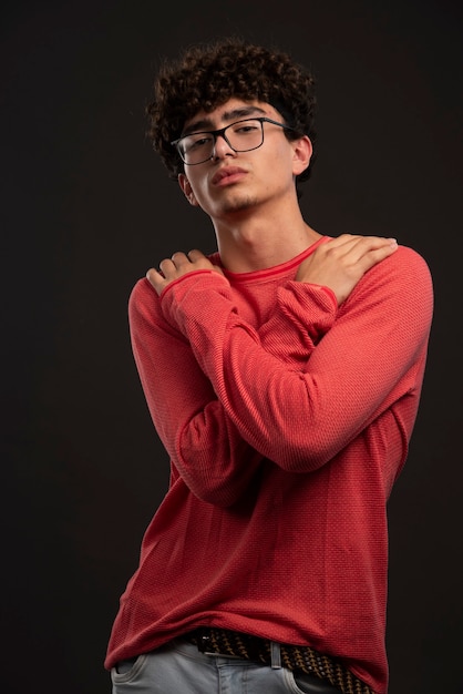 Giovane modello in camicia rossa con gli occhiali da vista e incrociando le braccia.