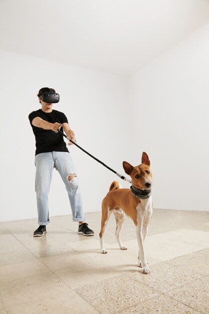 VR 안경, 청바지 및 가죽 끈에 basenji 개를 들고 빈 검은 색 티셔츠의 젊은 모델