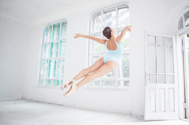 Young modern ballet dancer jumping on white wall