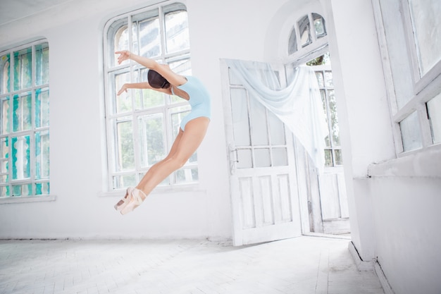 Young modern ballet dancer jumping on white wall