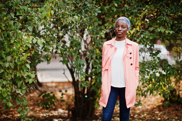 Free photo young modern fashionable attractive tall and slim african muslim woman in hijab or turban head scarf and pink coat posed at park