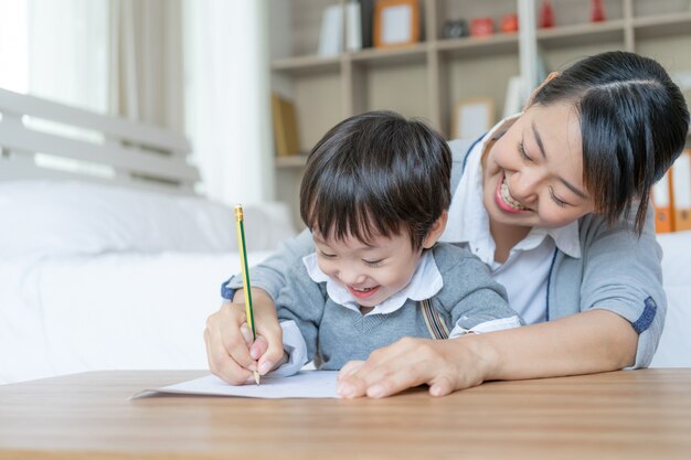 Молодая мама поймала сына за руку, держа карандаш, чтобы записать корь на белой бумаге, дошкольного дома