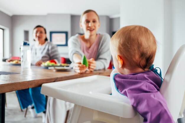 Молодая мама кормит своего ребенка твердой пищей в столовой