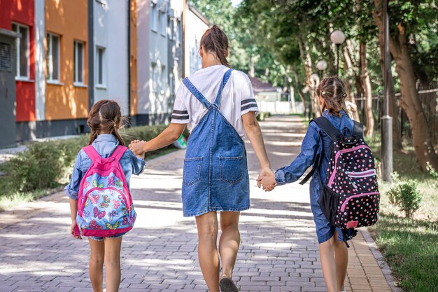 若いお母さんは小さな女の子を学校に連れて行きます、後ろ姿。