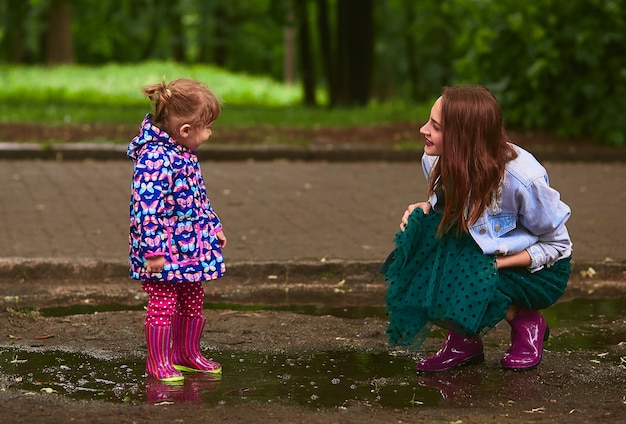 Free photo young mom and little daughter have fun walking in gumboots on the pools in park