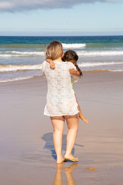 팔에 아이를 들고 바다 해변에서 작은 딸과 함께 여가 시간을 보내는 젊은 엄마