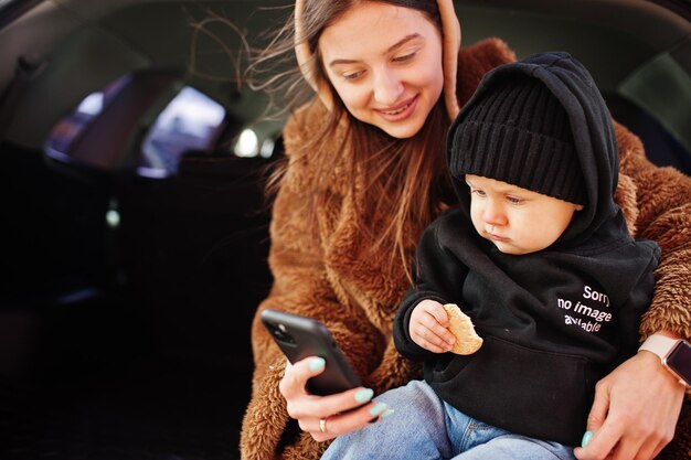 車のトランクに座って携帯電話を見ている若い母と子安全運転の概念