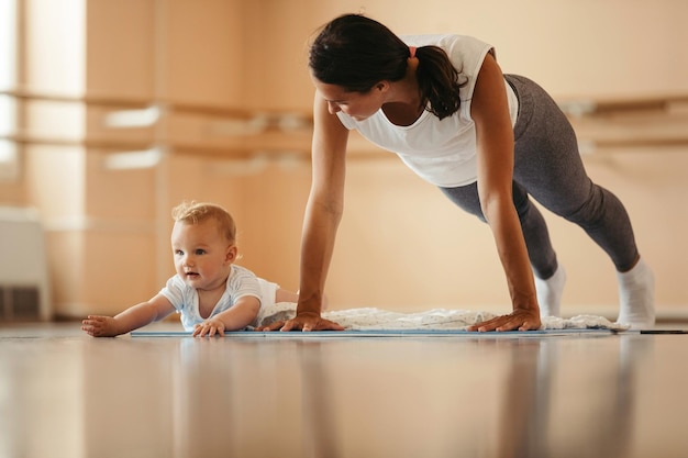 Giovane madre che esercita flessioni mentre è in allenamento sportivo con il suo bambino copia spazio