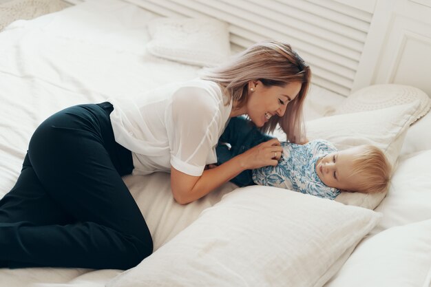 Young mother having fun laughing playing funny active games with cute child son in bedroom