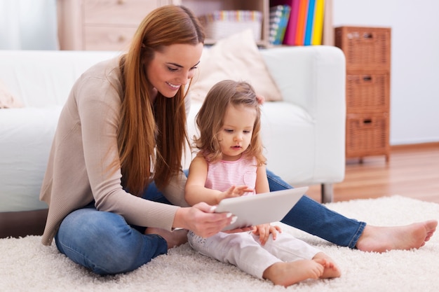 Молодая мать помогает дочери с цифровым планшетом