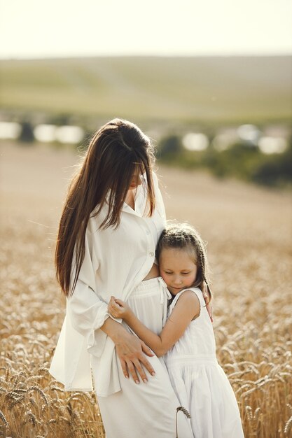 young mother and her daughter in white clothes  at the wheat field on a sunny day.