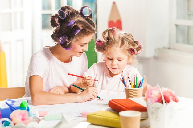 The young mother and her little daughter drawing with pencils at home