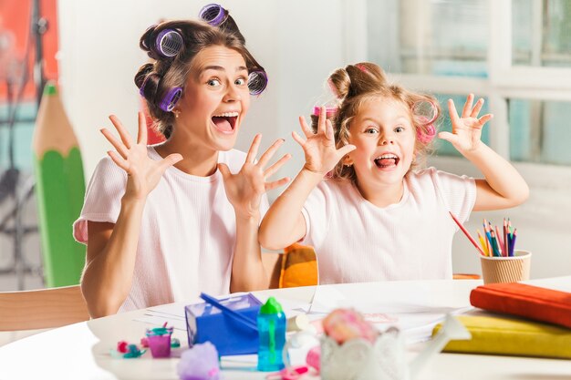 The young mother and her little daughter drawing with pencils at home