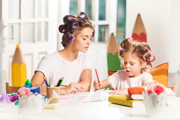 young mother and her little daughter drawing with pencils at home