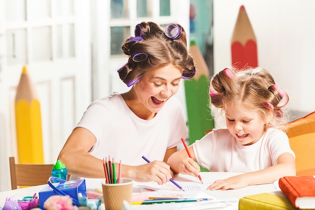 若い母親と彼女の小さな娘が家で鉛筆で描く
