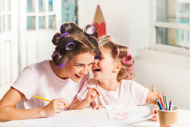 The young mother and her little daughter drawing with pencils at home