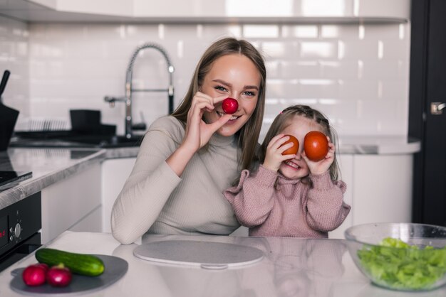 若い母親と子供の健康的な食品を準備し、キッチンで楽しんで