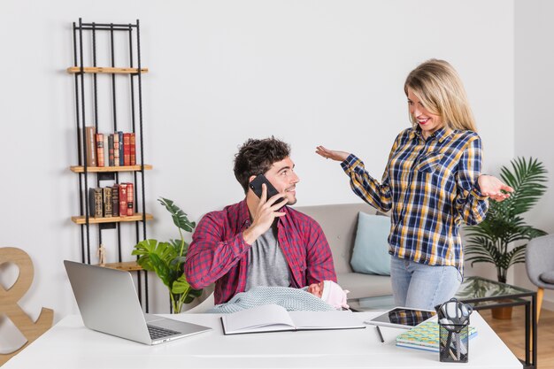 Young mother looking at father with baby talking on phone 