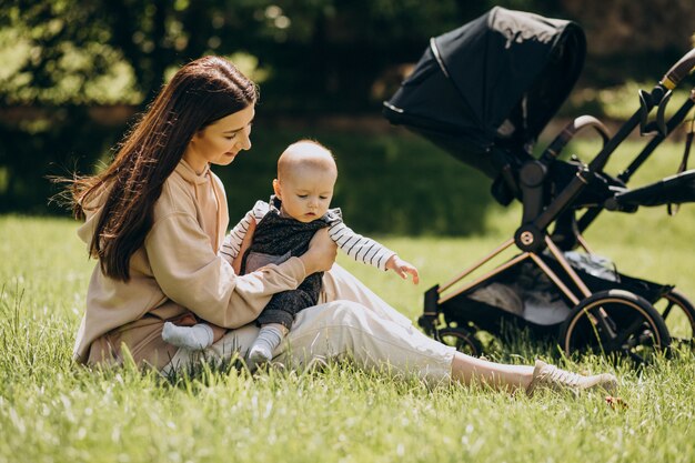 草の上に座っている彼女の赤ちゃんと一緒に公園で若い母親