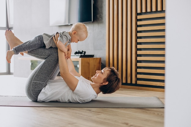 Young mother practice yoga with her toddler son on mat