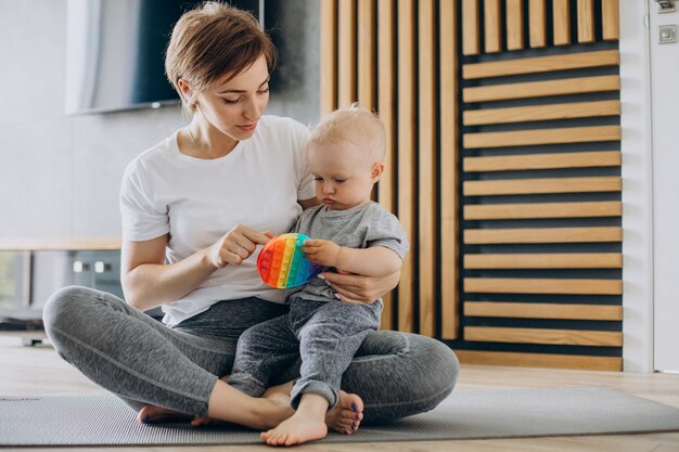 若い母親はマットの上で彼女の幼児の息子と一緒にヨガを練習します